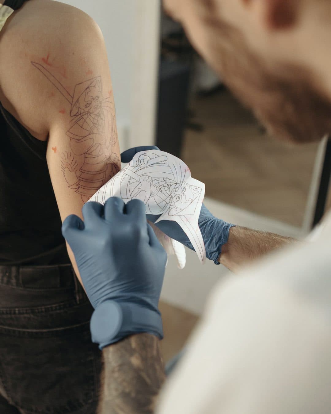 A tattoo artist peels a stencil off a client’s upper arm before the session starts