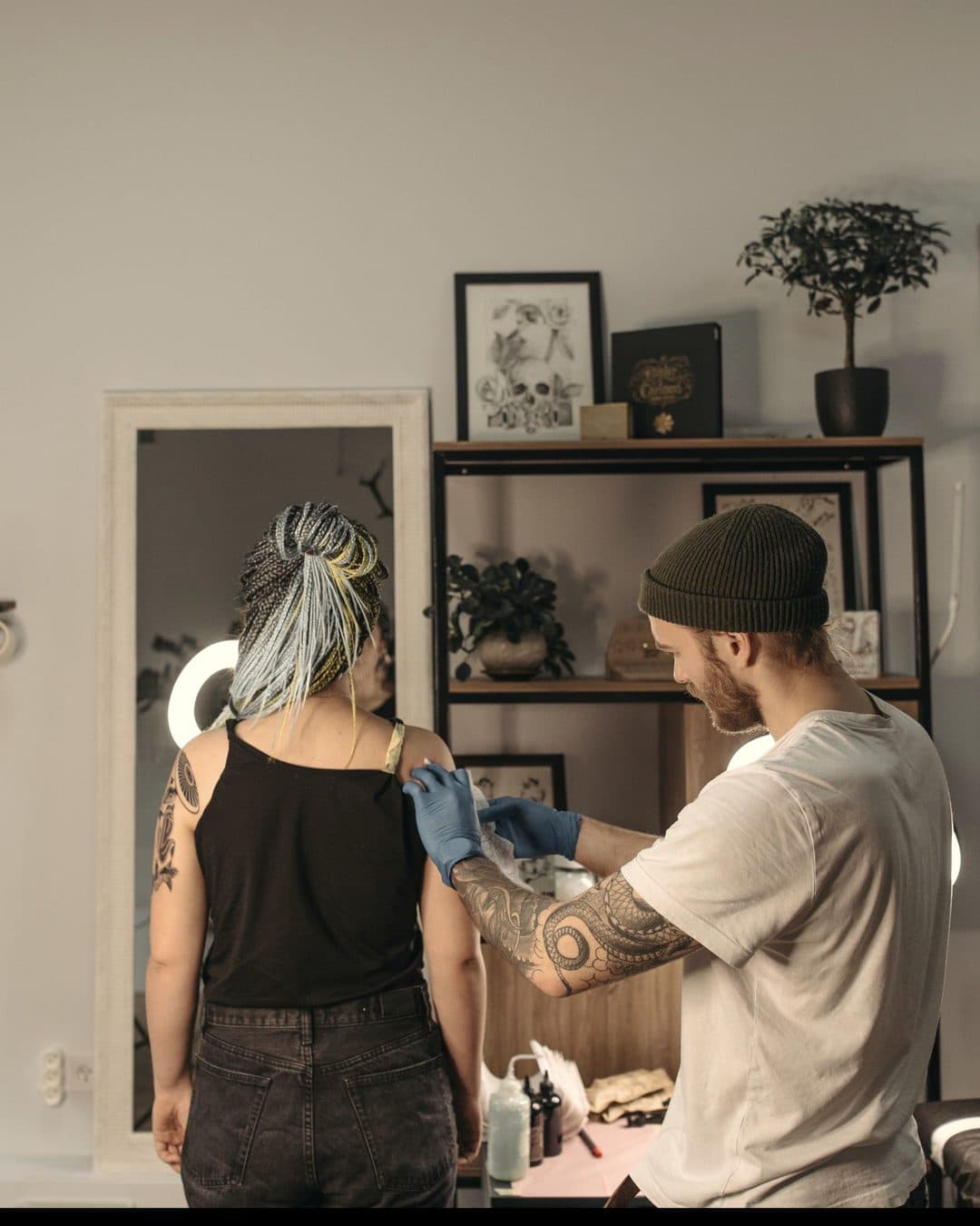 En tatuerare placerar en schablon på en kunds axel i en ljus studio